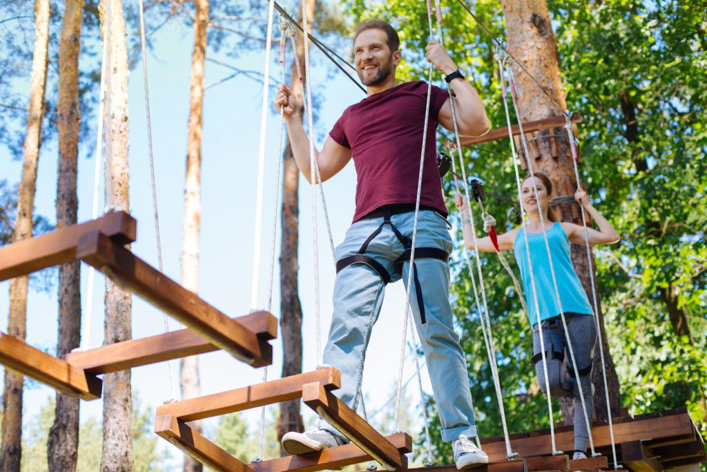 smiling husband and wife walking across a rope bridge